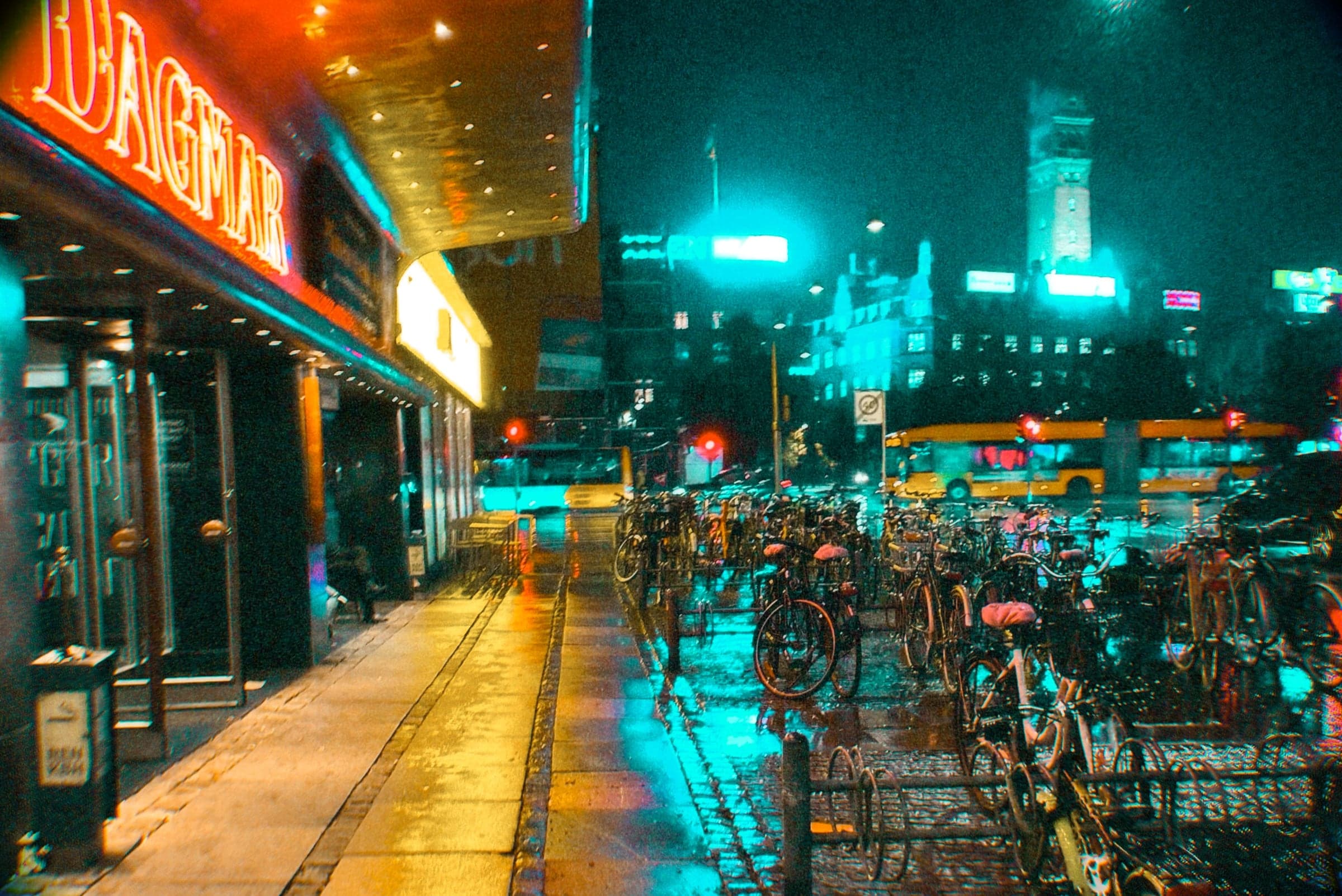 Neon signs and rows of bicycles on a wet street at night, Copenhagen